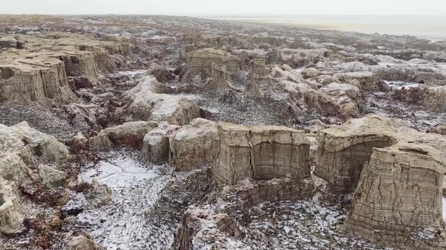 Aerial view of the Danakil Desert featuring unique salt formations and rugged volcanic terrain under a hazy sky in Dalol, Afar, Ethiopia.
