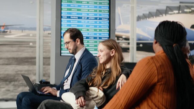 Talking, waiting to catch plane and men with women sitting on chairs in busy airport terminal. Chatting, trolleys and diverse tourists on metal benches before boarding departure gate opens