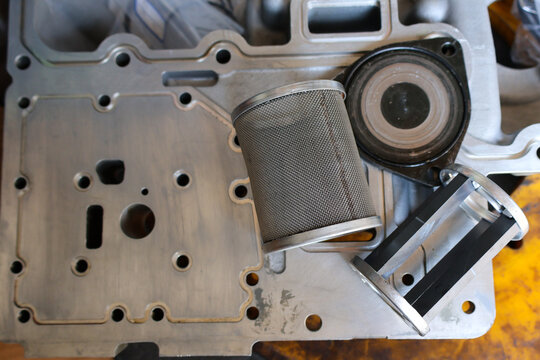 Detailed close up of a stainless steel mesh filter element with a machined aluminum hydraulic housing plate on a workshop table. High quality metal components for industrial filtration system.