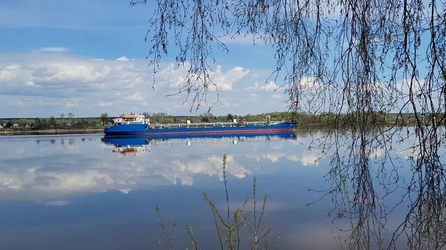 A cargo ship, a barge, and a tanker are traveling along the spring river.