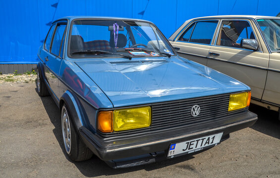 Blue first generation Volkswagen Jetta with distinctive yellow headlights and custom wheels. The classic sedan is parked outdoors during a vintage car exhibition