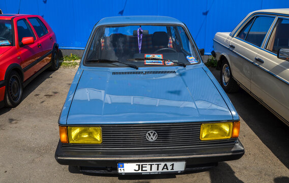 Blue first generation Volkswagen Jetta with distinctive yellow headlights and custom wheels. The classic sedan is parked outdoors during a vintage car exhibition