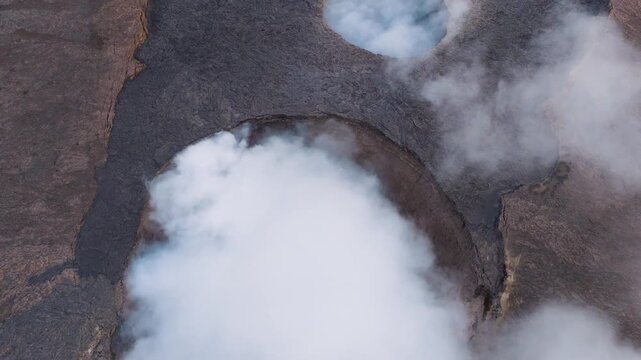 Aerial view of thick white smoke and steam billowing from the active crater of Erta Ale Volcano surrounded by dark volcanic rock and lava fields in Danakil Desert, Afar, Ethiopia.