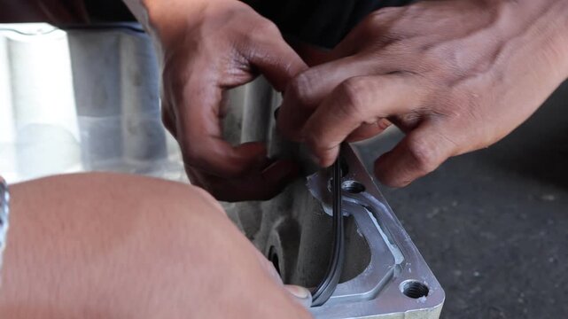 ​A professional mechanic manually installs a new black rubber gasket seal onto a metal engine oil pan component during a vehicle maintenance and repair process in an automotive workshop.