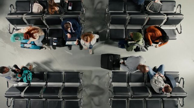 Rushing, top down view and travelers in busy airport with people killing time on chairs. Waiting for plane, high volume passenger flow concept and tourists with trolleys navigating hub next to people