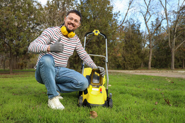 Naklejka premium Young man with lawn mower showing thumb-up outdoors