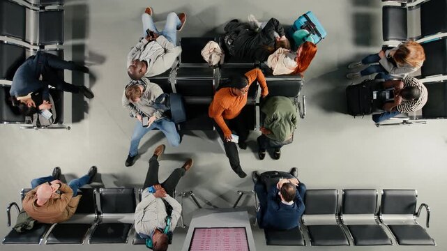 Top down view of passengers in airport napping after cancelled flights. Tired travelers sleeping on chairs after losing flight due to airline overbooking, red departure board screen high angle shot