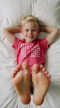 Young boy in pink t-shirt lying on white bed sheets showing feet to camera overhead view