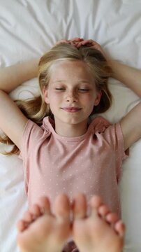 Young girl in pink polka dot shirt lying on white bed sheets, high angle view
