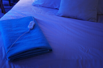 Folded electric heating pad on bed in dark room © Pixel-Shot
