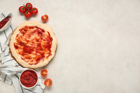 Pizza dough with tasty sauce and tomatoes on light background