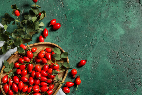 Wooden plate with fresh rose hip berries and leaves on green background