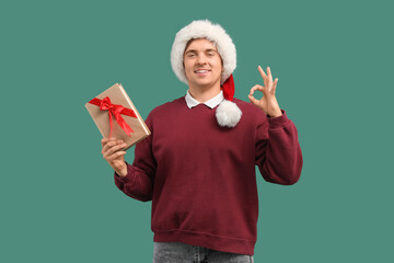 Naklejka premium Young man in Santa hat and with book showing OK on green background