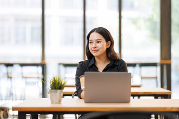 Obraz premium Pretty cheerful Asian business woman using laptop computer for remote work, managing her business, or studying online, showcasing productivity and professional concentration in a calm office environme