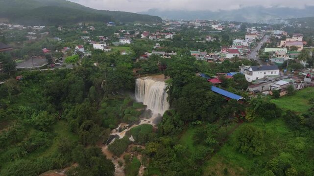A majestic white statue of Guanyin stands tall amidst lush green hills at Linh An Pagoda in Da Lat, Vietnam. The serene figure overlooks a Buddhist temple complex, offering a spiritual sanctuary.