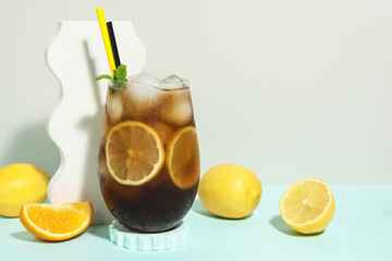 Naklejka premium Glass of Long Island iced tea cocktail with mint and citrus fruits on blue table against grey background