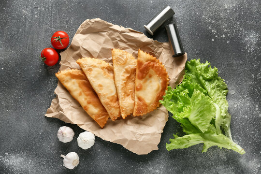 Parchment with tasty chebureks and fresh vegetables on grey grunge table