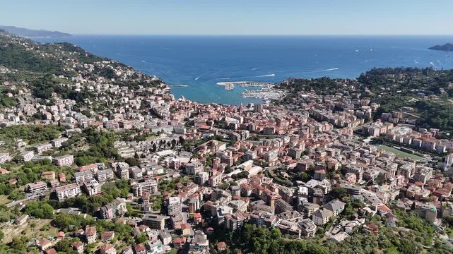 Aerial view of the coastal town of Rapallo featuring the harbor, colorful buildings, and lush green hills under a clear blue sky Rapallo, Liguria, Italy.