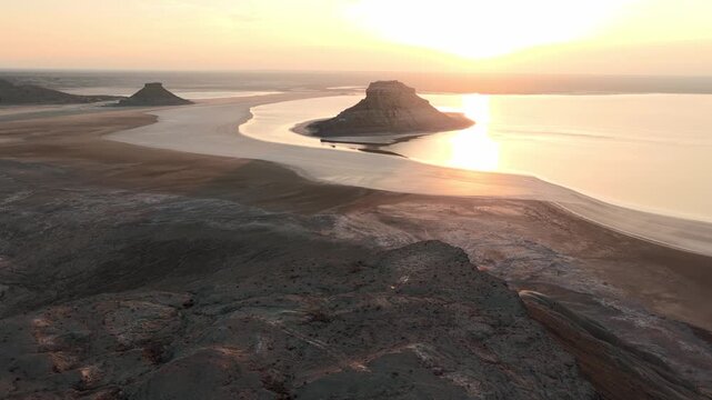 Aerial view of Karynzharyk hollow with its iconic buttes and salt flats under a golden sunset in Karakiya District, Mangystau Region, Kazakhstan.