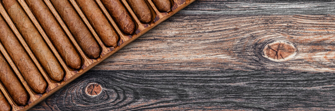 Cigars lined up on a wooden tray with a rustic finish in a warm setting for a social gathering