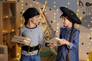 Naklejka premium Cute children dressed as pirates with books at home in evening