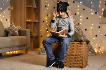 Naklejka premium Shocked boy dressed as pirate reading adventure book at home in evening