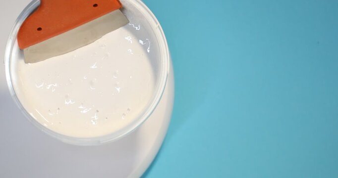 Bucket of plaster and putty knife spinning on light blue background, top view