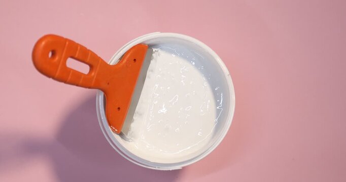 Bucket of plaster and putty knife on pink background, top view. Camera spinning