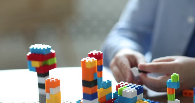 Construction toy. Little boy playing with building blocks at table indoors, closeup. Camera moving in