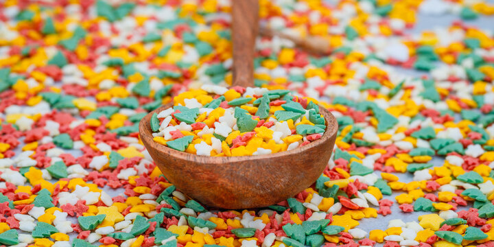 Colorful sprinkles in various shapes scattered on a table with a wooden spoon full of decorations used for desserts