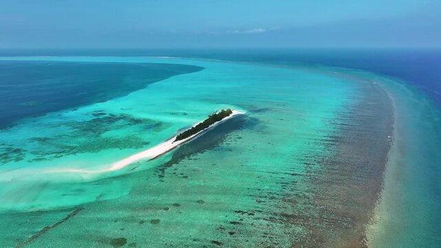 Aerial view of a narrow tropical island with lush green palm trees surrounded by turquoise coral reefs and deep blue ocean water in Fulhadhoo, Baa Atoll, Maldives.