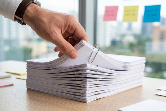 Person organizing a large stack of blank white reports with metal paperclips