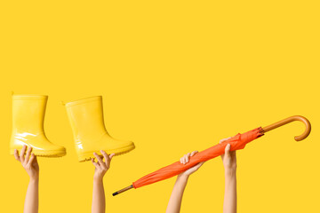 Female hands with stylish umbrella and gumboots on yellow background © Pixel-Shot