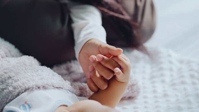 Softly blurred background shows two hands touching gently. One hand, small and delicate, rests atop another. Fingers interlace with care, suggesting warmth and safety. The scene evokes quiet intimacy