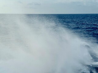 Naklejka premium Abstract view of ship wake trailing behind a moving vessel, showing foamy white water patterns blending into deep blue ocean, with soft horizon line creating minimalistic maritime background