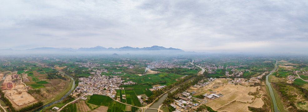 A historic British-era irrigation canal winding through the lush green wheat fields of rural Khyber Pakhtunkhwa, Pakistan, while a heavy morning fog settles over the landscape, 12k panorama