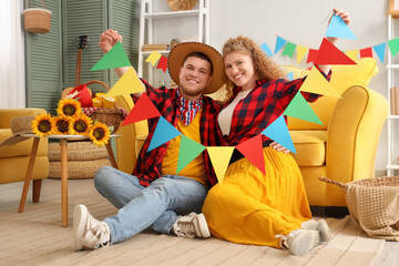 Obraz premium Happy young couple with colorful flags at home. Festa Junina celebration