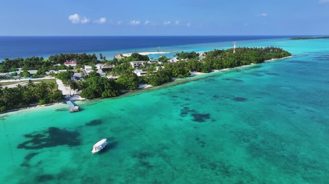 Aerial view of a tropical island featuring white sand beaches, lush palm trees, and a boat in turquoise waters Fulhadhoo, Baa Atoll, Maldives.