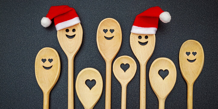 Wooden spoons with smiley faces and Christmas hats on a dark surface during holiday season