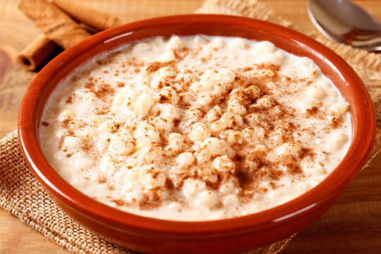 A bowl of creamy white corn porridge sprinkled with cinnamon, served with peanut and coconut candy in a rustic setting. Popular traditional Brazilian dish.