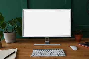 Fototapeta premium Modern computer, houseplant and notebook on wooden table near green wall
