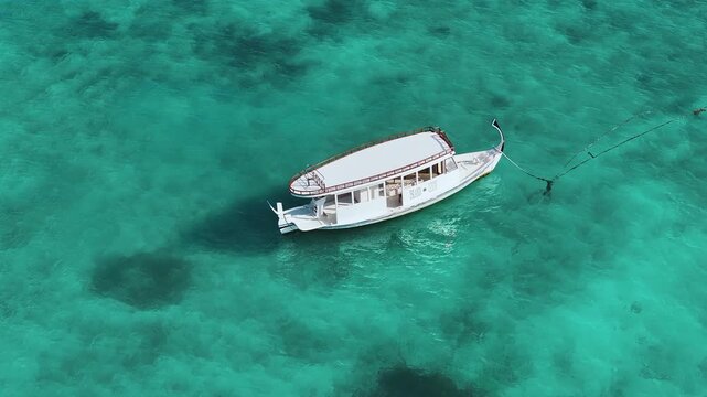 Aerial view of a traditional white dhoni boat anchored in the crystal clear turquoise waters in Fulhadhoo, Baa Atoll, Maldives.
