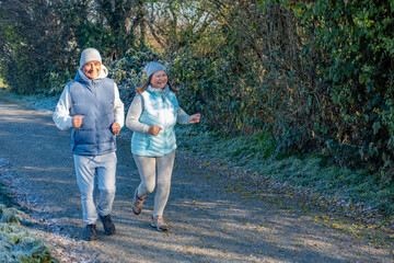 Fototapeta premium happy senior couple jogging on frosty path, cool weather, morning jog, active lifestyle, healthy enjoying active aging together sports, fitness during, healthier routine in nature, daily exercise