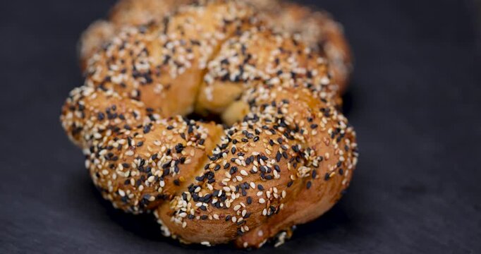 Golden braided simit with sesame seeds, this traditional Turkish simit is sprinkled with black and white grains on a black natural slate background.