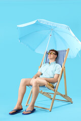 Young man resting in deck chair on blue background