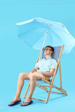 Young man resting in deck chair on blue background