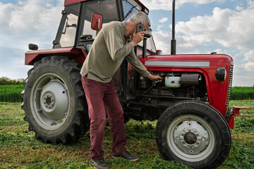 Senior farmer repairing tractor on the field calling for help or getting advice over the phone © phoenix021