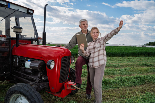 Daughter improving her fathers farming by using technology holding tablet and talking, man leaned on a tractor looking ahead 