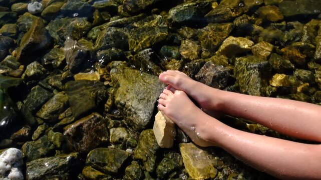 Teenager girl relaxing in water, barefoot in clear cool water. Healthy lifestyle. Young woman enjoying nature on the beach. Ripple patterns reflect light on water over pebbles