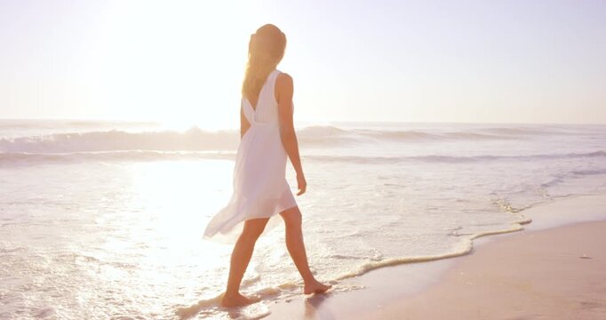 Woman, walk and summer holiday by ocean with waves, sunset and tropical getaway for weekend break. Female person, travel and calm outdoor on beach with peace, wellness and island for vacation trip.